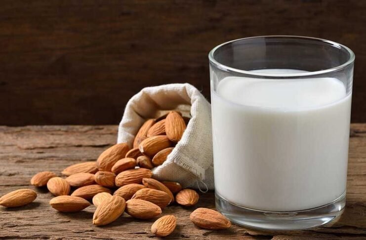 Glass of almond milk and raw almonds on dark background – almond milk benefits